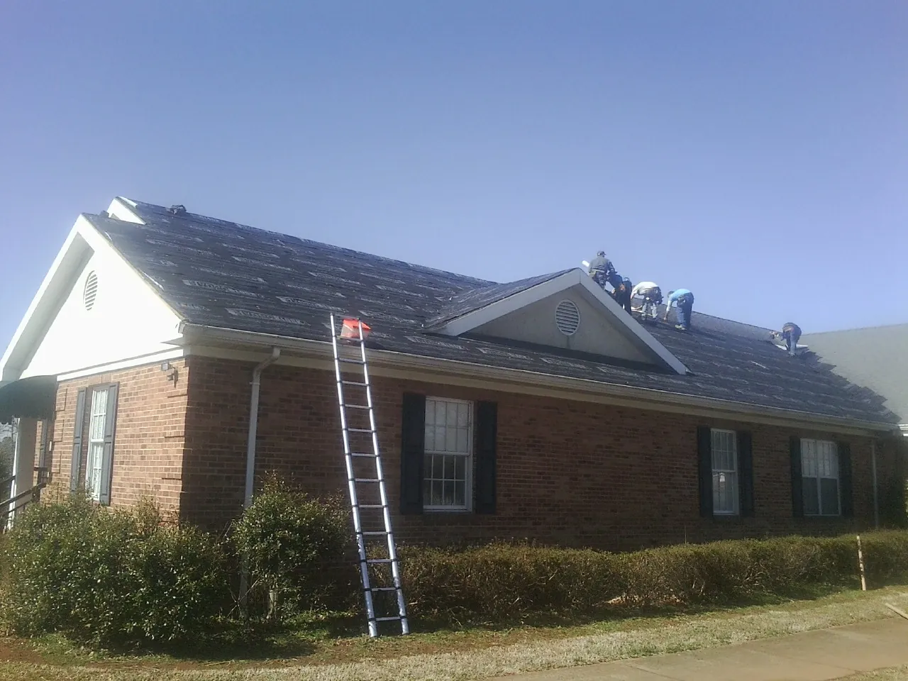 Crew tearing shingles off a brick ranch roof with a ladder set — Emergency Roof Repair work by our crew in Owensville