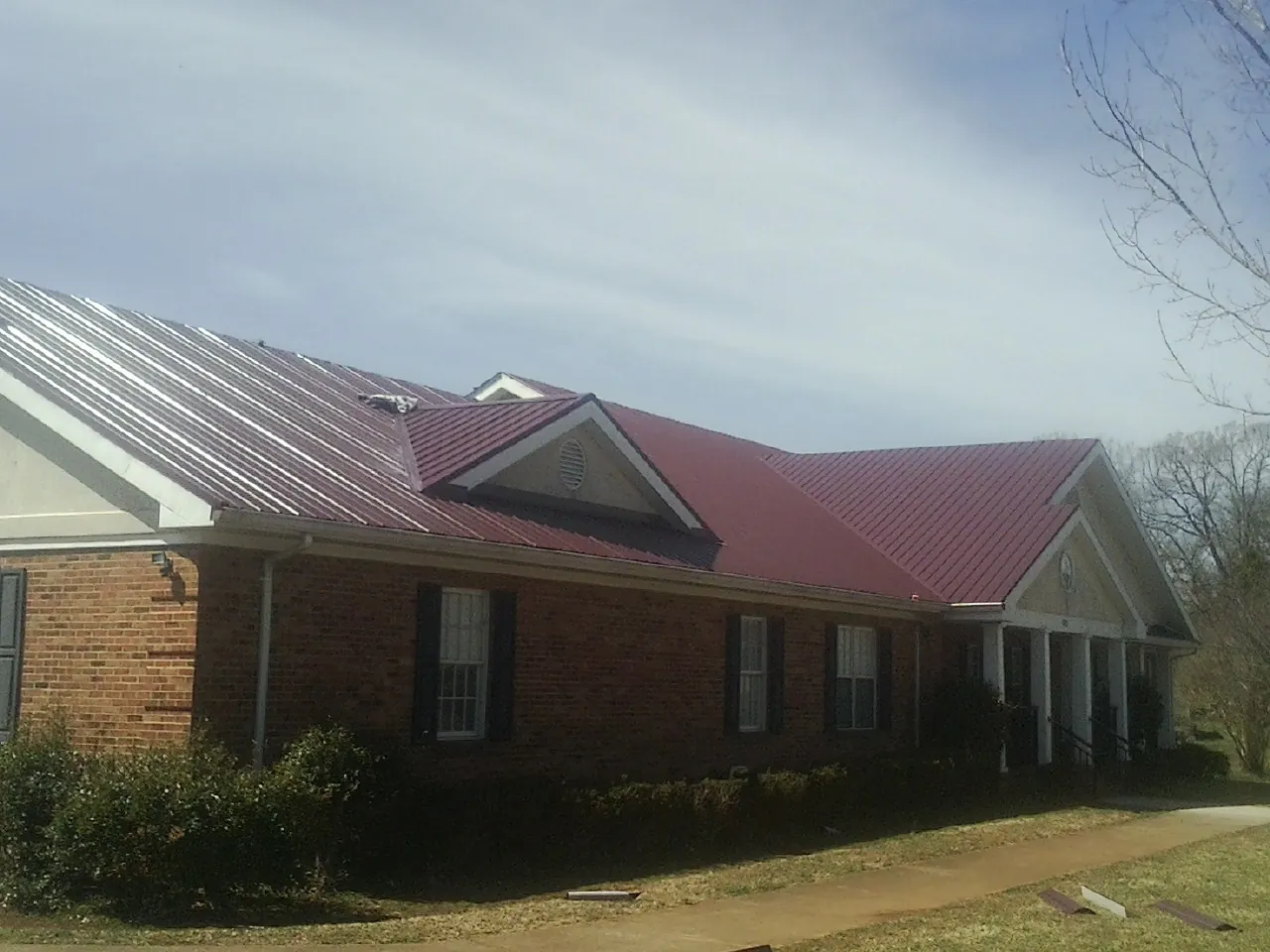 Red metal roof with gabled entries on a long brick building, from a Hail Damage Roof Repair job in Owensville